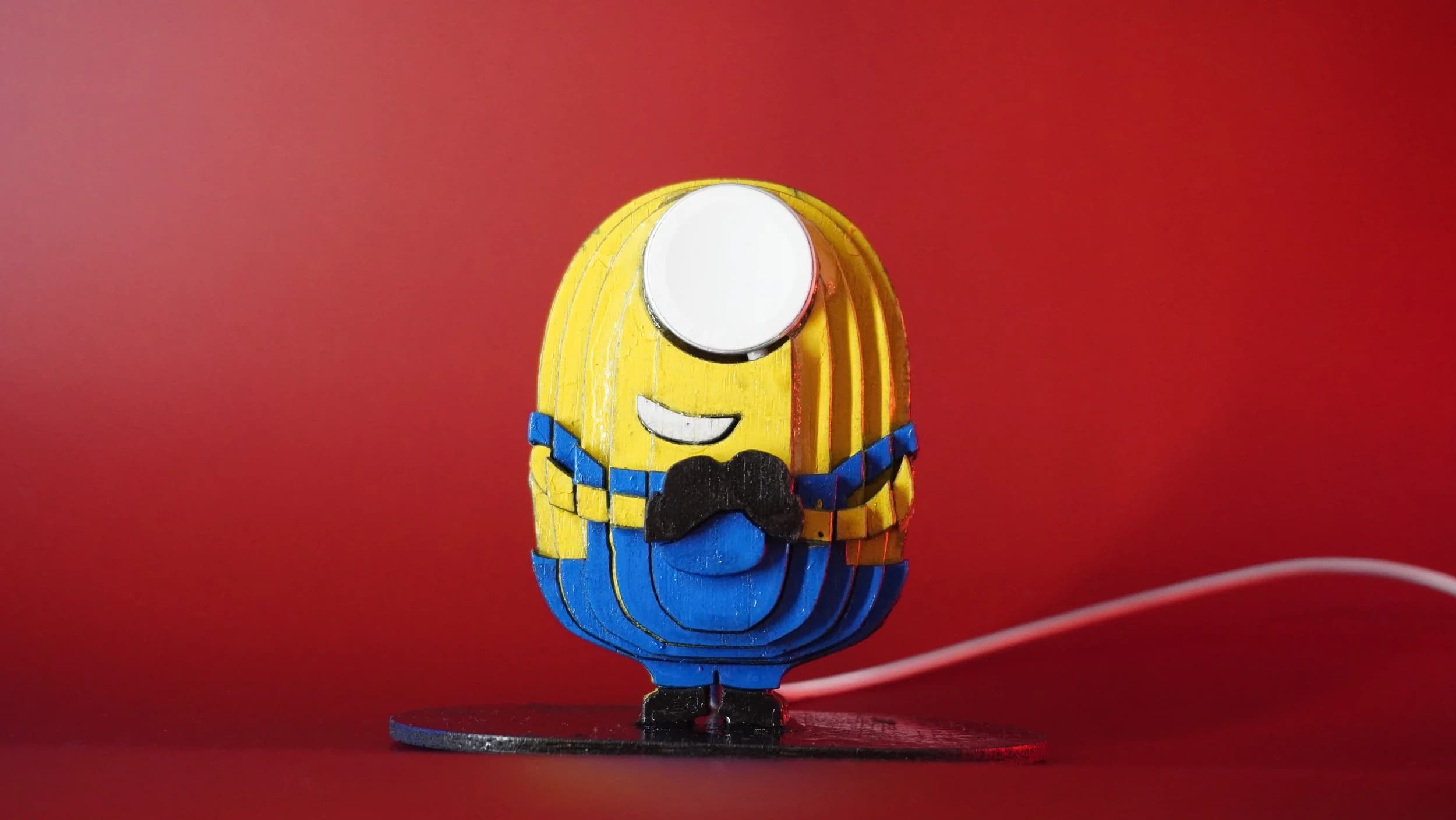 A minion apple watch charger. 3D made from painted layered plywood with the charger embedded. The apple watch serves as the minion's goggles. A video of this design + build is also available on Pinewood Slurpy.